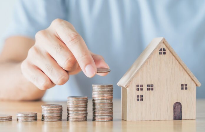 Man hand put coin on coins stack with wooden house on wood table